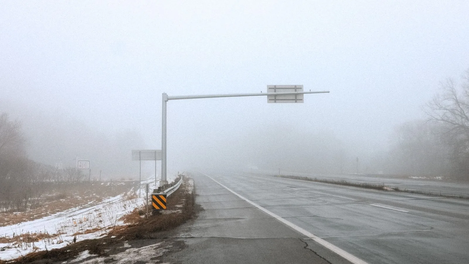 A misty winter road with traffic signs and snow on the roadside in Des Moines, Iowa, daytime